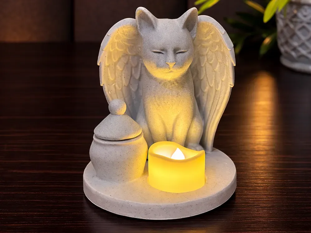 Gato de asas em acabamento pedra sobre base oval, com uma urna pequena ao lado e uma vela de LED acesa