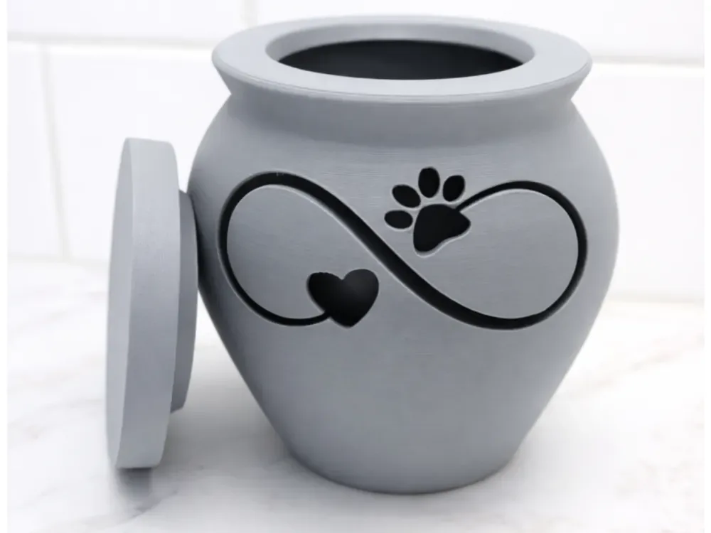 Urna pet cinza em formato de vaso, com símbolo do infinito, coração e marca de pata vazados, tampa apoiada ao lado
